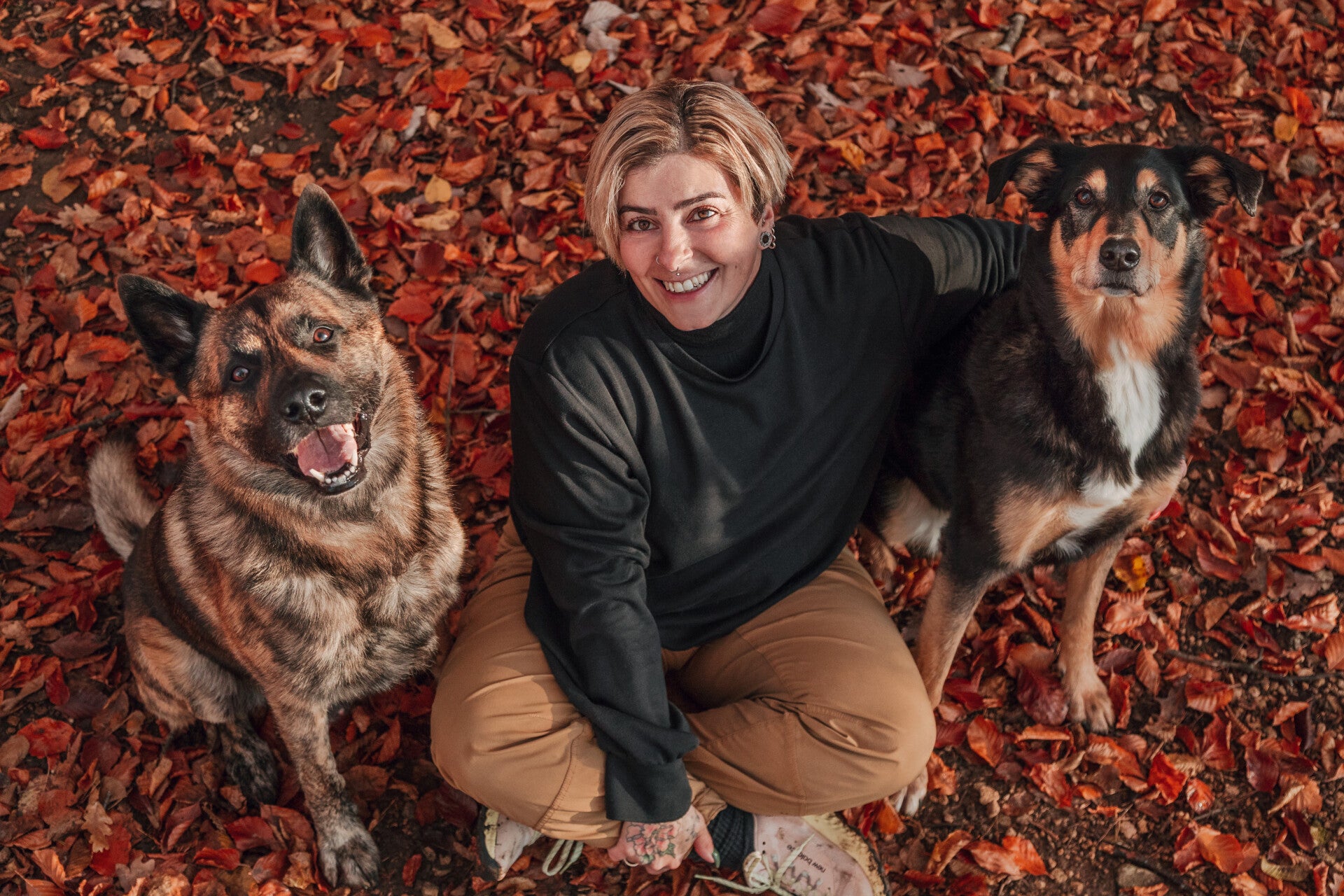 Tanja Hänggi sitzt lachend im Herbstlaub zwischen ihren Hunden Nero und Mia
