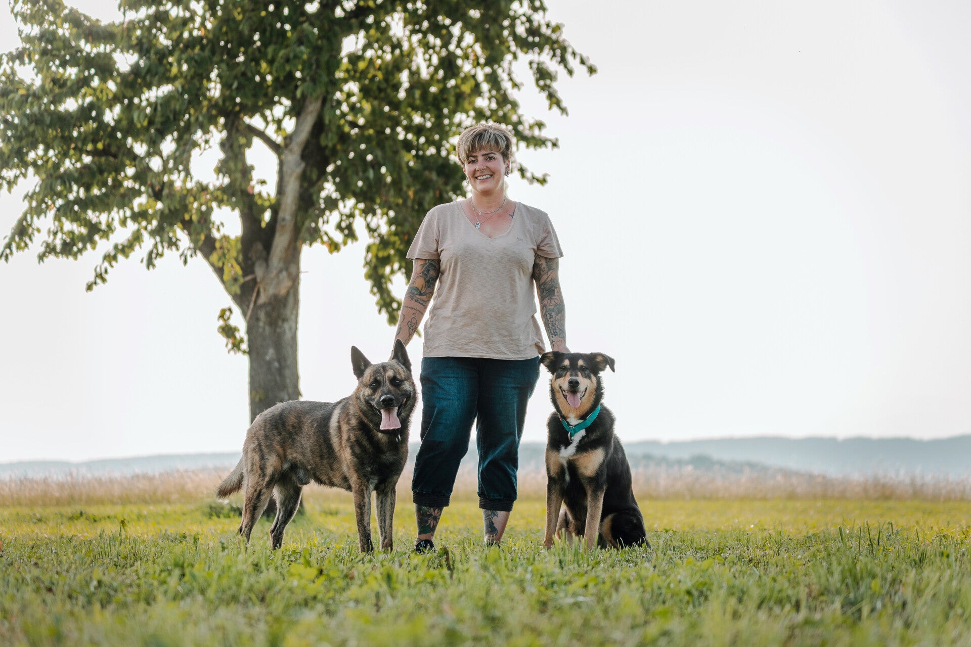 Tanja Hänggi steht mit ihren beiden Hunden auf einer Wiese unter einem Baum